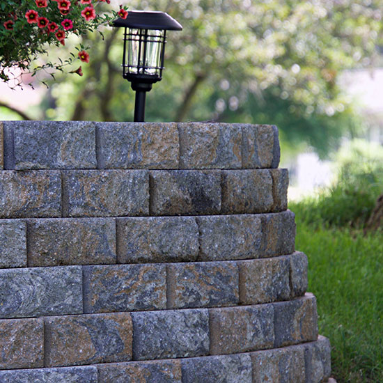 A retaining wall with small solar light on top next to red flowering bush